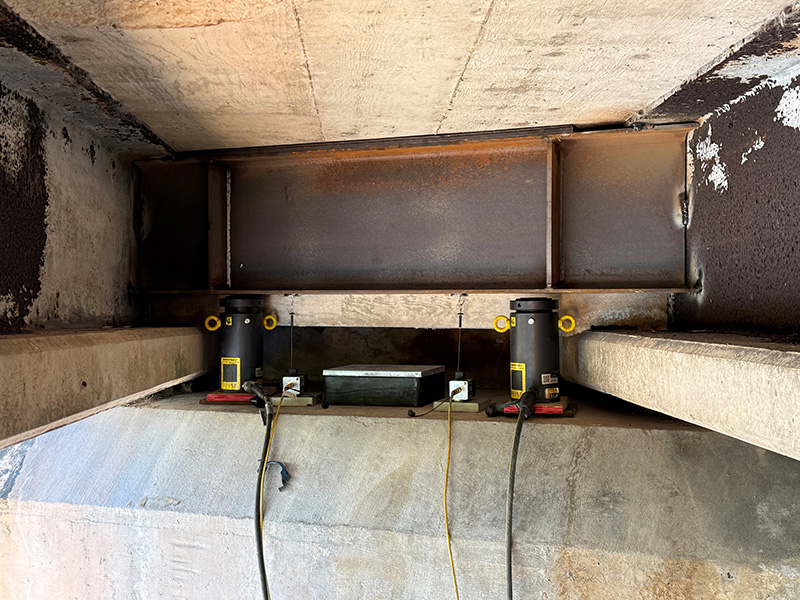 Custom fabricated beam and lock-ring cylinders with stroke sensors installed under a girder on the Glebe Road overpass in Bermuda.