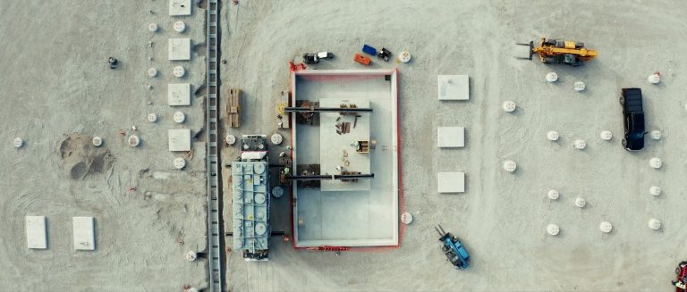 Aerial view of a 187-ton power transformer as it prepares to travel across a containment pit to its concrete pad during the construction of a solar farm's power station.